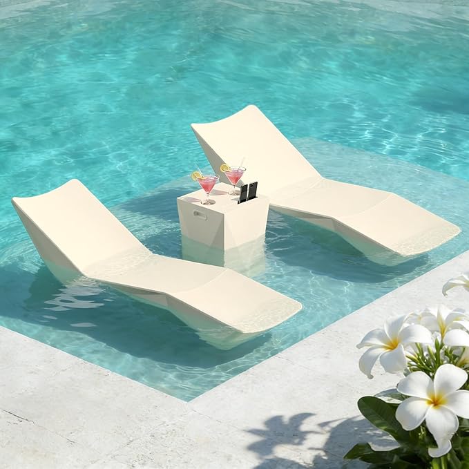 Two modern cream-colored floating lounge chairs in a turquoise swimming pool, with a small matching side table between them holding two cocktails. White flowers are visible in the foreground corner.