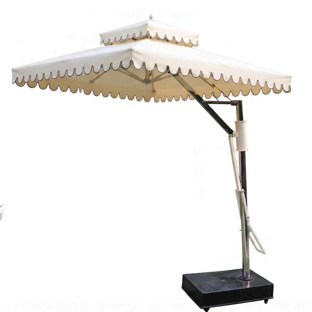 A two-tiered cantilever patio umbrella with cream-colored fabric canopy and scalloped edges, supported by a silver metal pole with a black weighted base, isolated on a white background.