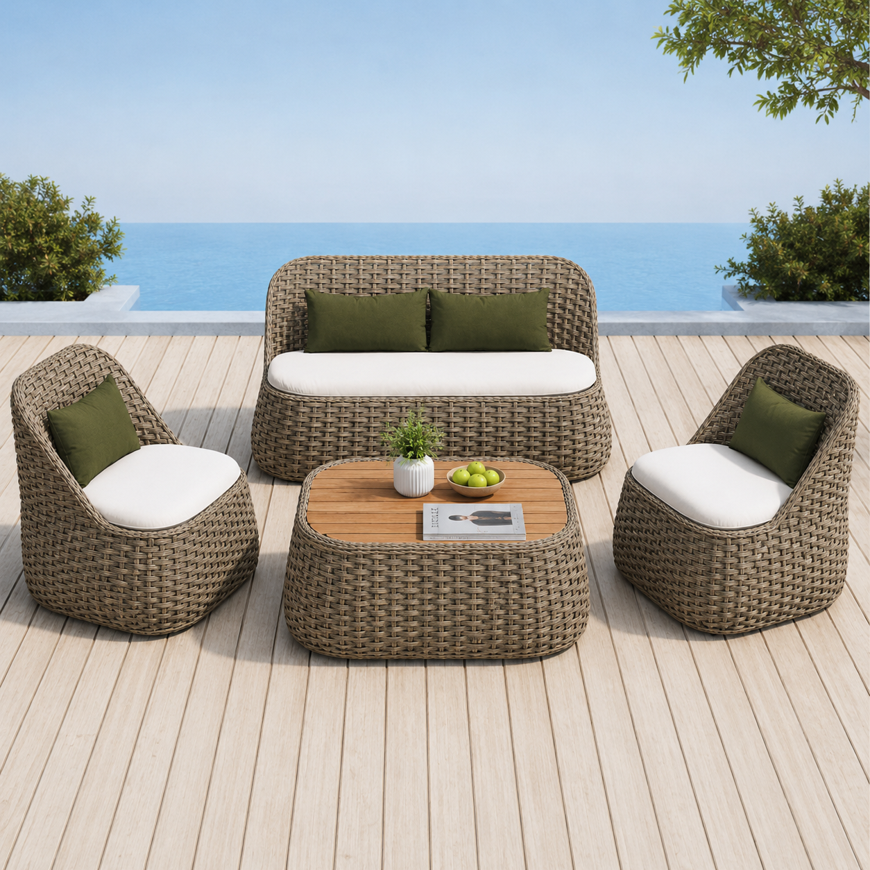 A 4-piece outdoor patio conversation set on a light wood deck overlooking the ocean. The set includes a 3-seat sofa, two armchairs with white cushions and green pillows, and a low coffee table with a light wood top.