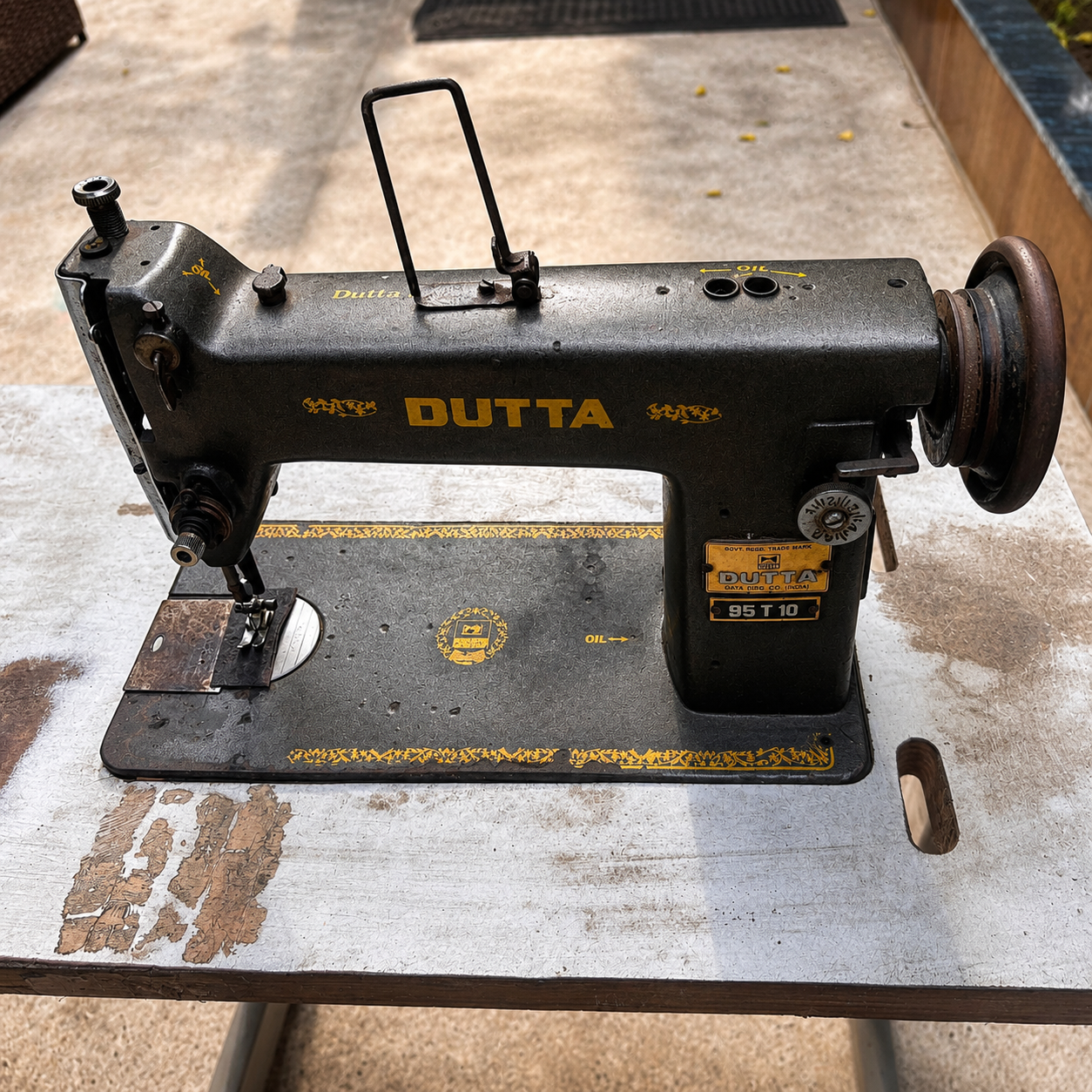 A vintage Dutta BST-15 sewing machine in black with yellow lettering, resting on a weathered metal table.